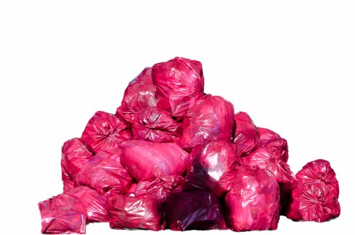 A large pile of bright pink plastic rubbish bags, tightly knotted and stacked on top of each other, situated on a flat surface possibly outdoors or in a warehouse environment. The bags appear to contain general waste materials, with some bags showing slight creases and reflections on their glossy surface. The pile is arranged in a roughly triangular shape, with the bags at the base providing a stable foundation and smaller bags towards the top. The background is plain and neutral, emphasizing the vibrant colour of the rubbish bags. This image visually represents collection or disposal of waste, consistent with rubbish removal services offered by Commercial Waste Abbots Langley, serving local businesses and residents in the area around Abbots Langley postcode.